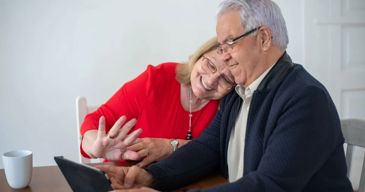 Elderly couple smiling while using a tablet for a video call at home